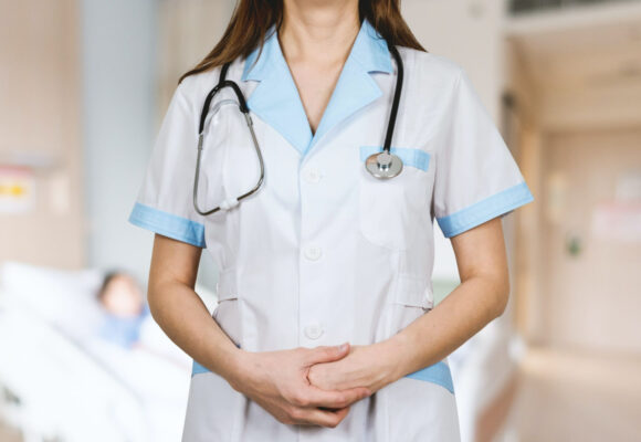 Healthcare professional in a white coat with a stethoscope, standing with hands clasped