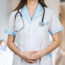 Healthcare professional in a white coat with a stethoscope, standing with hands clasped